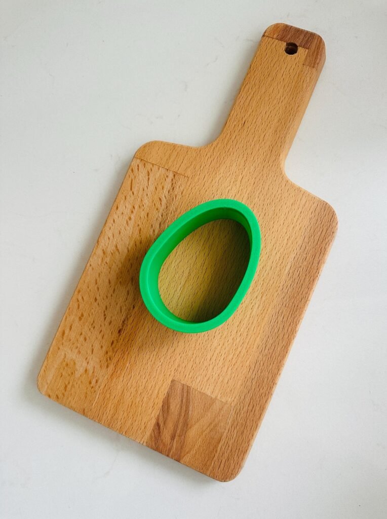 Green egg shaped cookie cutter on a cutting board.